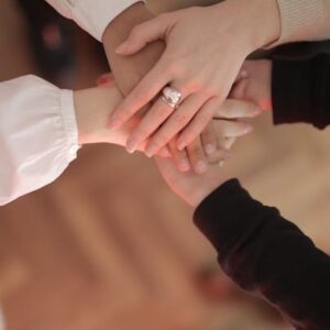 Top view of faceless friends in different clothes stacking hands together while standing on wooden floor indoor on sunny day